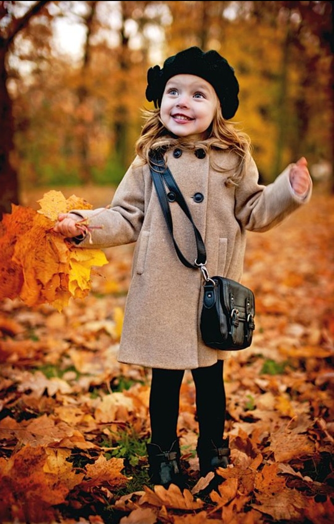 girls thanksgiving outfit, smiling female toddler, wearing a beige winter coat, black leggings and a black hat, with a black cross body bag