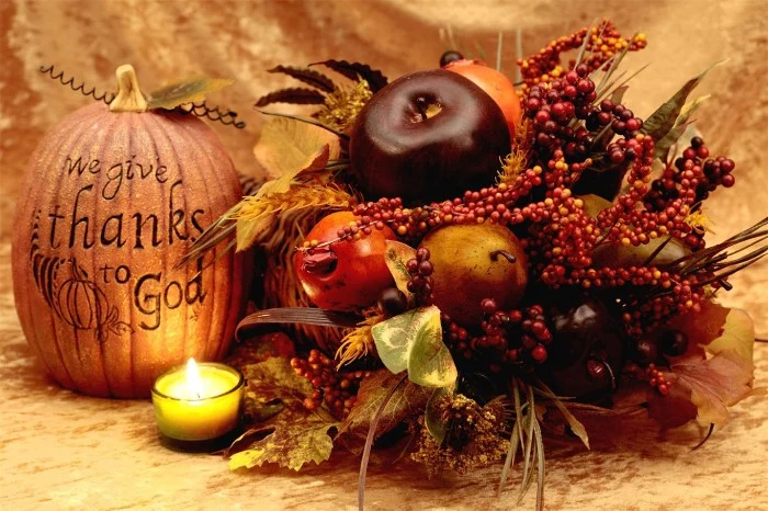 we give thanks to god, carved on a faux pumpkin, placed near a small lit candle, and a fall-themed decorative arrangement
