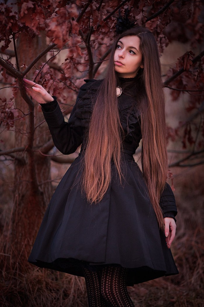 slim young woman, with long brunette hair, wearing a frilly, black gothic lolita dress, with a cameo brooch