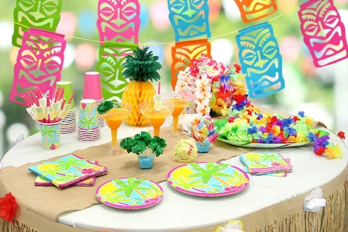 50th birthday colors, hawaiian-themed party, with colorful tiki-mask garlands, and a table decorated with a paper pineapple, multicolored plates and orange cocktails