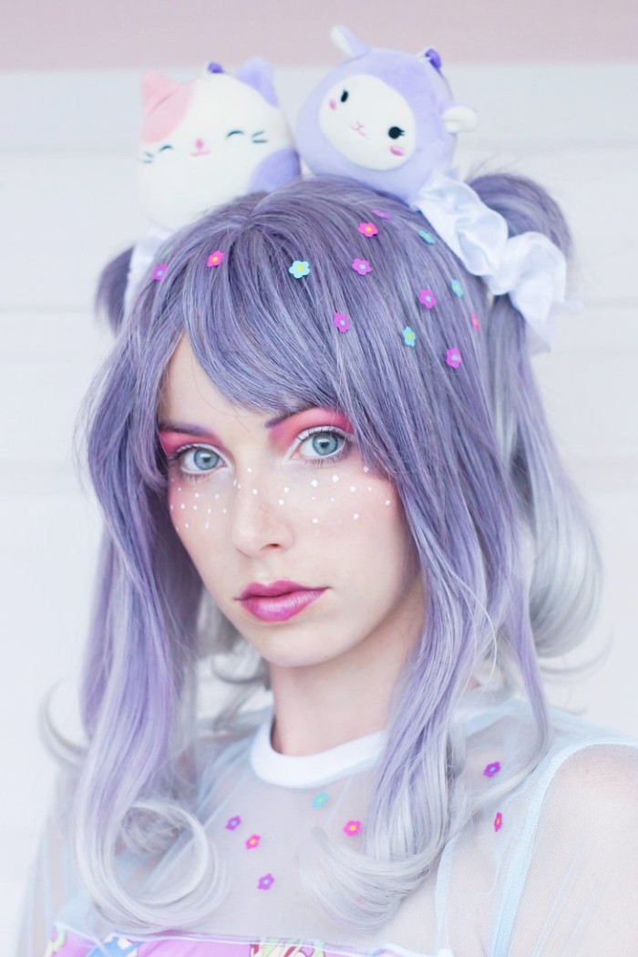 glossy pink lipstick, white and pink eye shadow, and white hand-drawn freckles, shaped like stars, on the face of a young woman, wearing a blue wig, what is lolita, two plush toys on her head