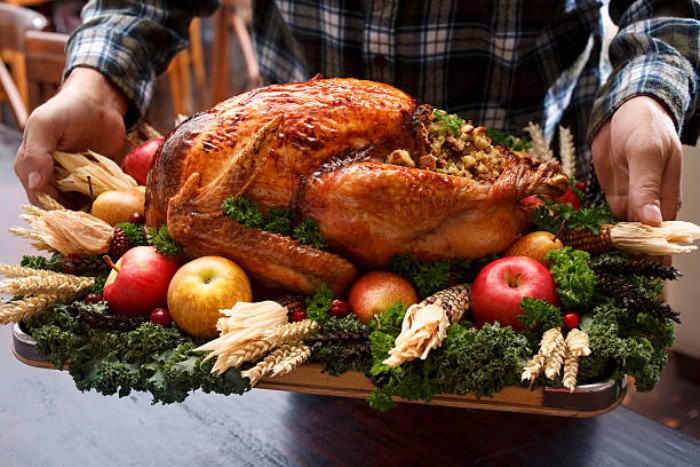 trey containing a large roasted turkey, on a bed of green vegetables, decorated with apples and corncobs, berries and dried wheat stalks, thanksgiving text messages, held by a man, dressed in a plaid shirt