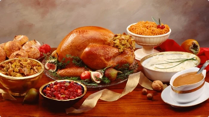 bread rolls and mashed potato, roasted turkey and several side dishes, thanksgiving greeting message, rustic wooden table