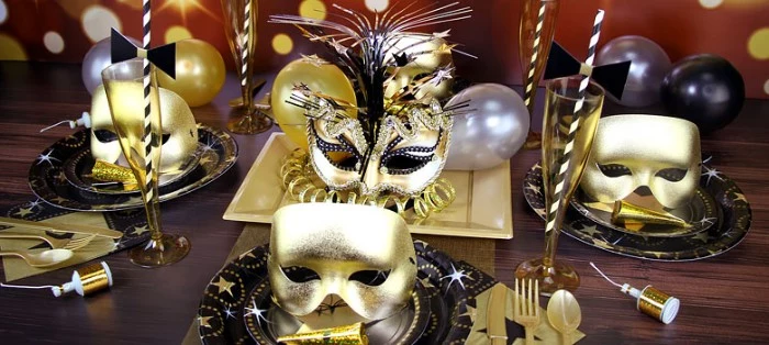 four venetain-style masks, in metallic gold, three plain and one decorated with flowers and glitter, on a table set for a party, 50th birthday ideas, masked ball theme