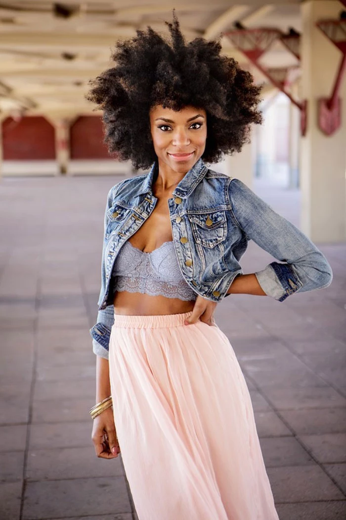 how to wear a bralette, smiling black woman, with an afro hairstyle, dressed in a pale pink maxi skirt, a light blue lace bralette, and a cropped denim jacket