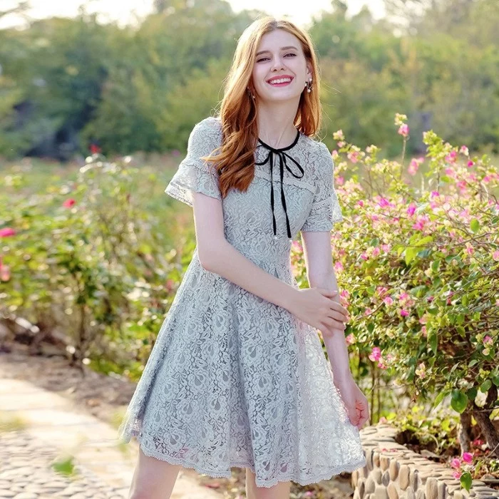 laughing slim young woman, with wavy ginger hair, wearing an off-white lace mini dress, with a black ribbon, what is lolita