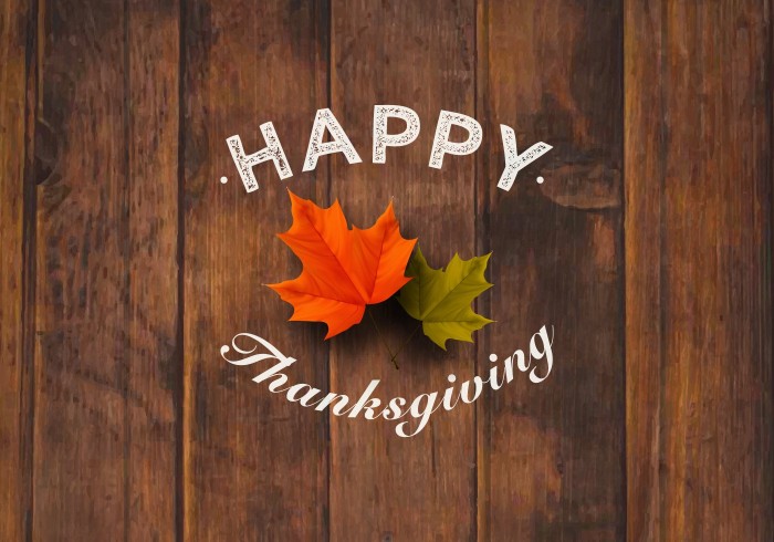 small green leaf, and a larger orange leaf, on a wooden surface, with the words happy thanksgiving, superimposed in white