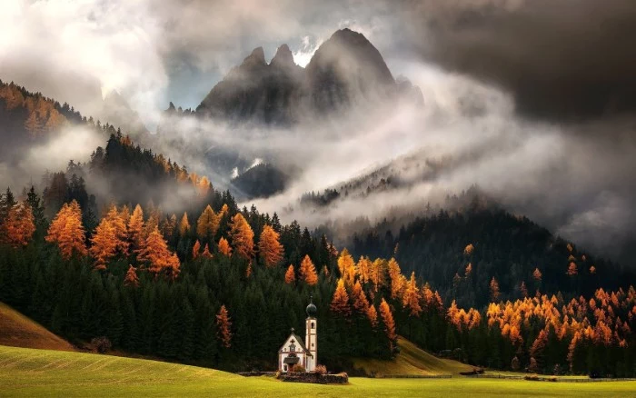 peak of a tall mountain, surrounded by white mist, happy thanksgiving wishes, hills covered in dark green, and bright orange trees, pale green meadow with a church