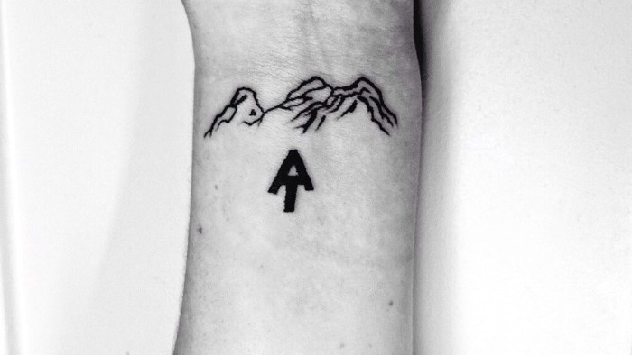 black minimalistic arrow head, pointing upwards to some mountains, tatooed in black, on a the wrist of a slim man, lower arm tattoos