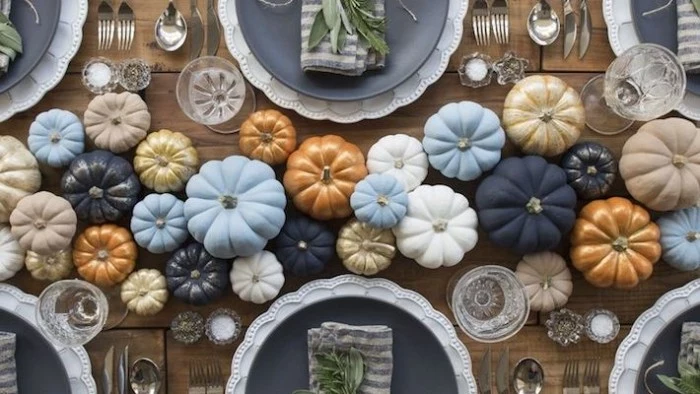 many faux pumpkins, in pale blue and dark navy, white and beige, orange and gold, decorating a wooden table, with large dark blue plates, cheap centerpiece ideas, seen from above