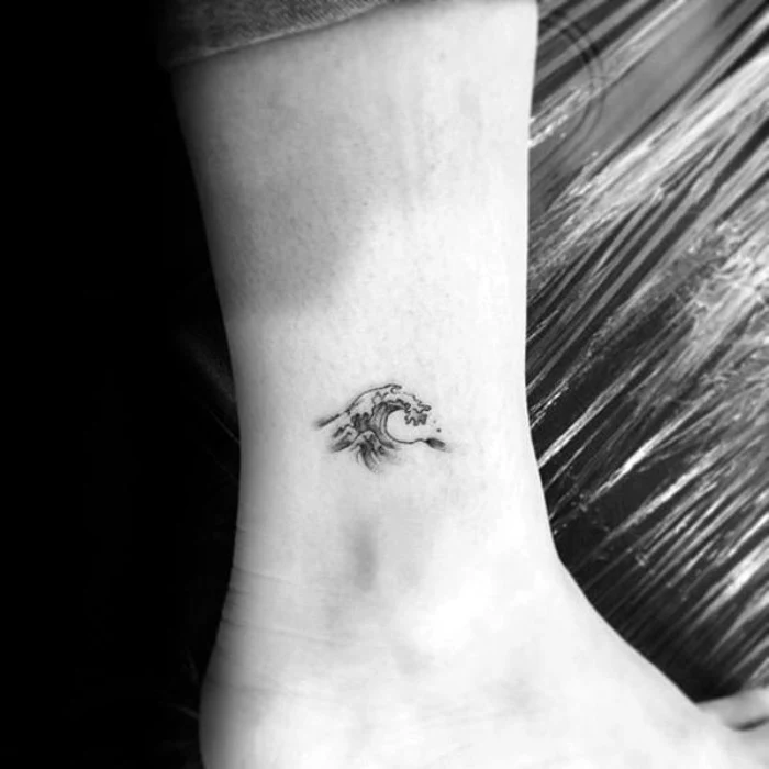wave tattooed in black, on a man's ankle, seen in close up, on a black and white photo, very small tattoo