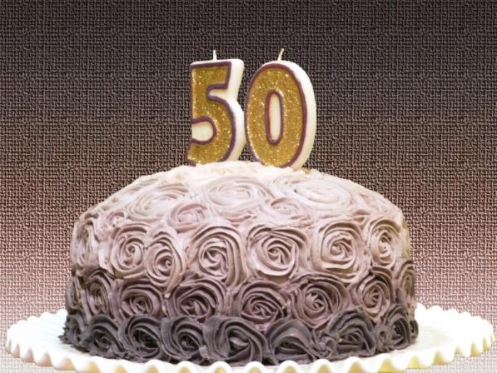 birthday cake in three shades of grey, with frosting shaped like multiple roses, and two candles covered in gold glitter, and shaped like the numbers 5 and 0
