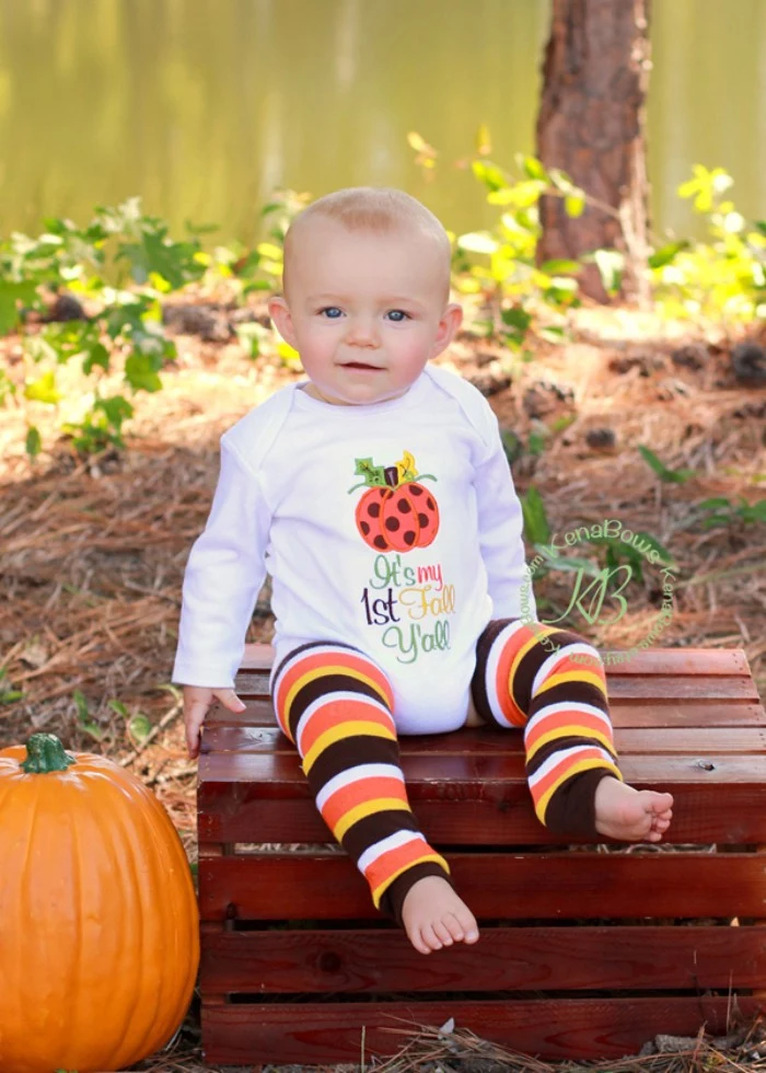 infant wearing a white onesie, with long sleeves, and a multicolored festive print, baby's first thanksgiving outfit, striped leggings in brown and yellow, white and orange