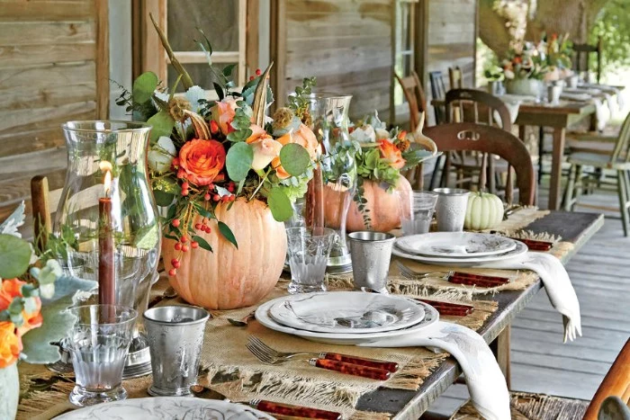outdoor wooden tables, decorated with pumpkins, filled with flowers, thanksgiving dinnerware, lit candles in glass vases, white dishes and napkins