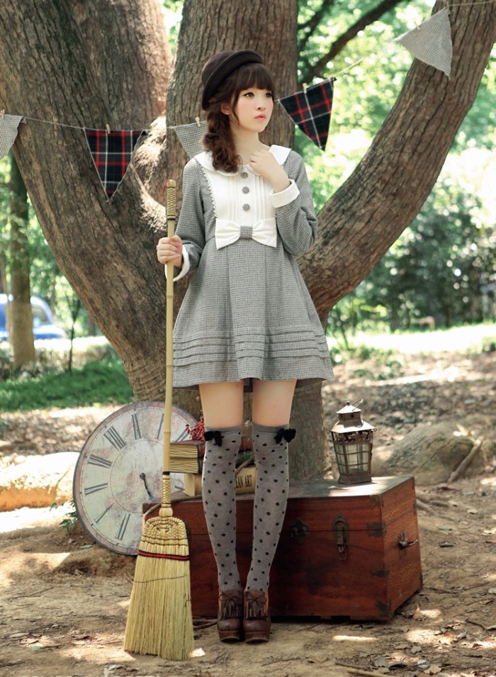 japanese lolita, in a light grey mini dress, featuring a white bib detail, a peter pan collar, and a bow on the waist line, grey over-the-knee socks, with black polka dots and bows