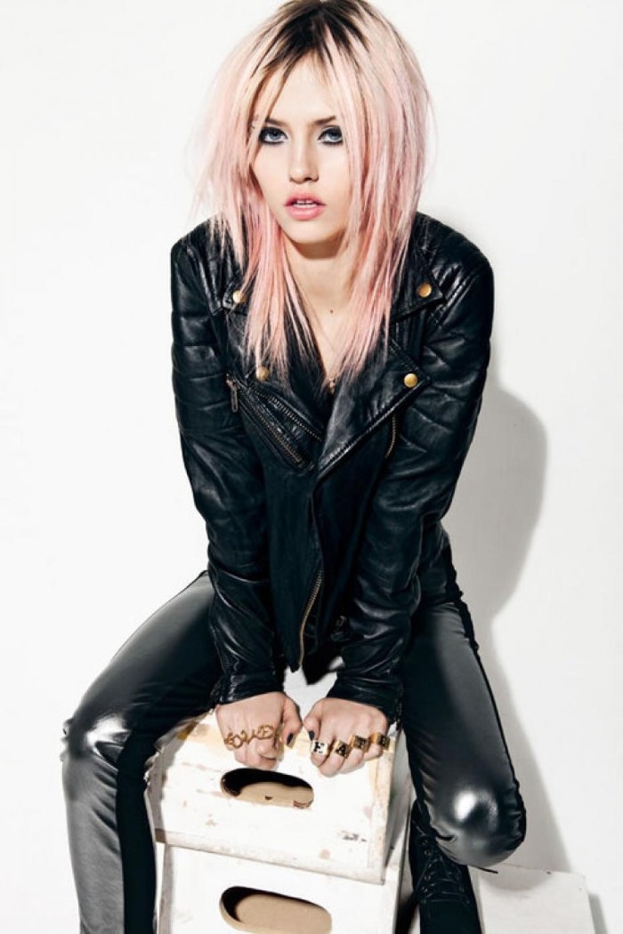 pink-haired young woman, with dark roots, sitting on some wooden crates, dressed in shiny black, skinny leather trousers, and a black leather biker jacket, 80s grunge or punk aesthetic