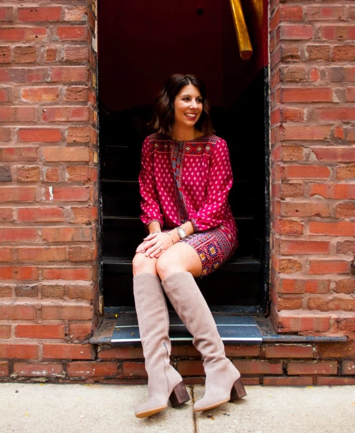 creamy grey tall suede boots, on a smiling brunette woman, with short wavy hair, dressed in a red patterned mini dress, comfy outfits for the holidays