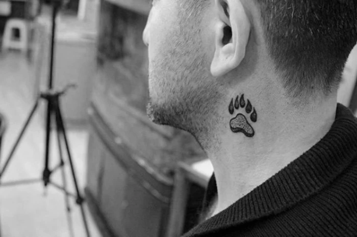 small symbolic tattoos, paw print with claws, tattooed in black, on the side of a man's neck, signifying strength and bravery