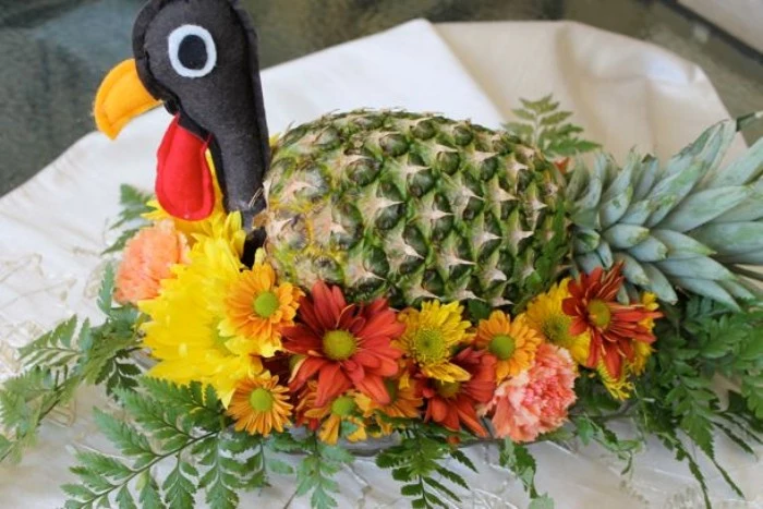 felt turkey head, attached to a pineapple, decorated with yellow, pink and orange flowers, and green fern leaves, creative turkey decorations 
