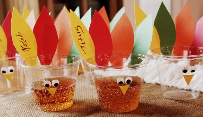 cups made out of clear plastic, decorated with eye stickers, and pieces of paper, in yellow and red, orange and green, turkey decorations for your party