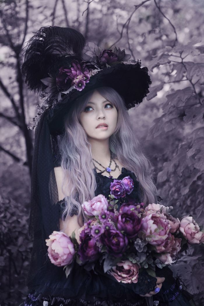 wavy platinum blonde hair, on a pale woman, wearing an extravagant black hat, with large feathers and faux flowers, black gothic dress, large bouquet of pale pink, and purple flowers