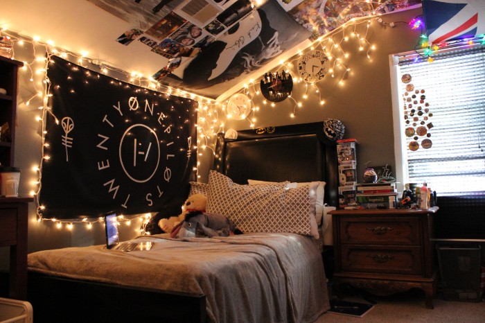 dark room decorated with lit string lights, various posters and a black, fabric wall hanging, teenage bedroom ideas for small rooms, wooden cupboard and a window