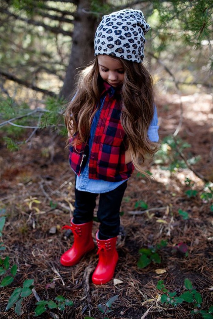 rubber rain boots in red, worn by a small girl, with dark blue jeans, a light chambray, a plaid red and blue gilet, and an animal print beanie hat, toddler thanksgiving outfit