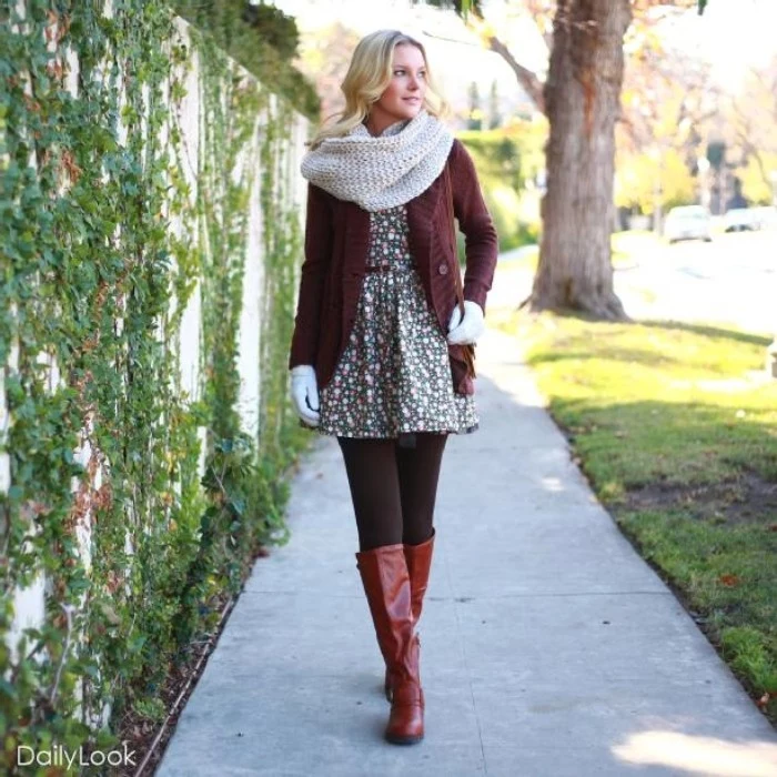 chunky knit off-white scarf, worn over a brown cardigan, and a ditsy mini dress, by a blonde young woman, thanksgiving outfits for women, tall dark red leather boots