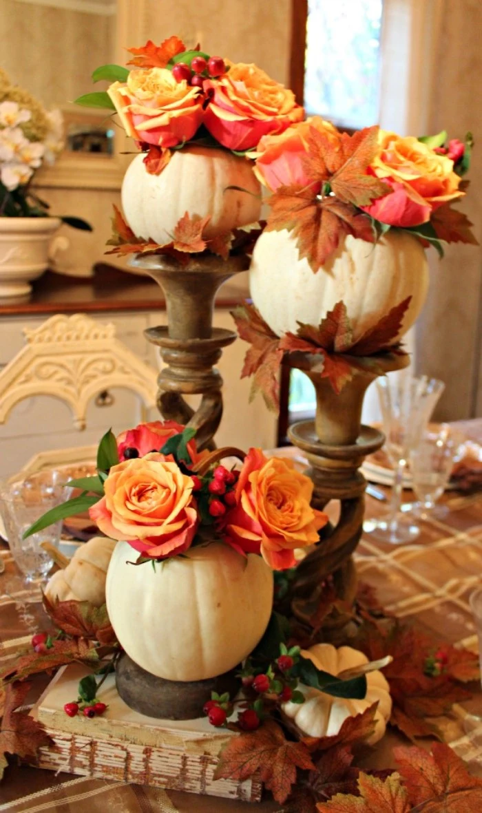 three small hollow white pumpkins, filled with orange roses, and brown fall leaves, and placed on ornamental stands