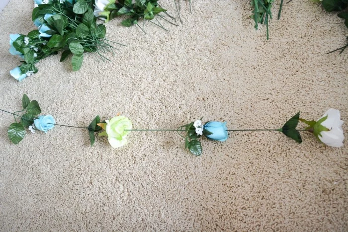 four fake flowers, with pale blue, light yellow and white blossoms, and long green stems, stuck together to form a column, diys for girls, more blue flowers in the background 