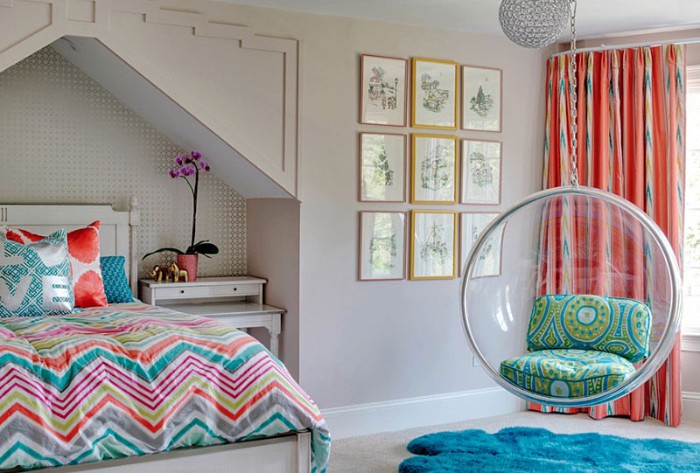 teen bedrooms, bed with a multicolored duvet, a round swing, made from clear plastic, window with orange patterned curtains, and nine framed artworks 