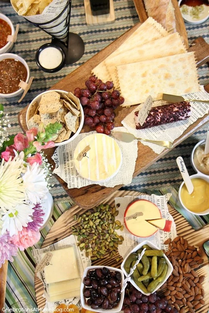 50th birthday themes, wine tasting experience, wooden boards containing different kinds of cheese, crackers and grapes, olives and pickles, on a table decorated with flowers
