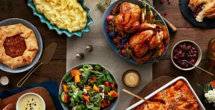 assorted dishes including two roasted chickens, muashed potato and salad, thanksgiving text messages, on a wooden table
