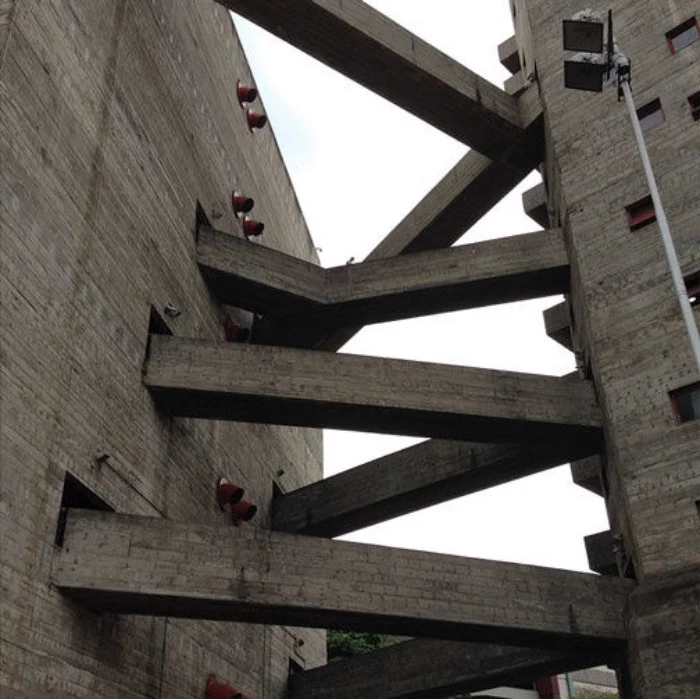 bridge-like concrete structures, connecting two grey buildings, brutalist design, featuring protruding pipes, and small square windows