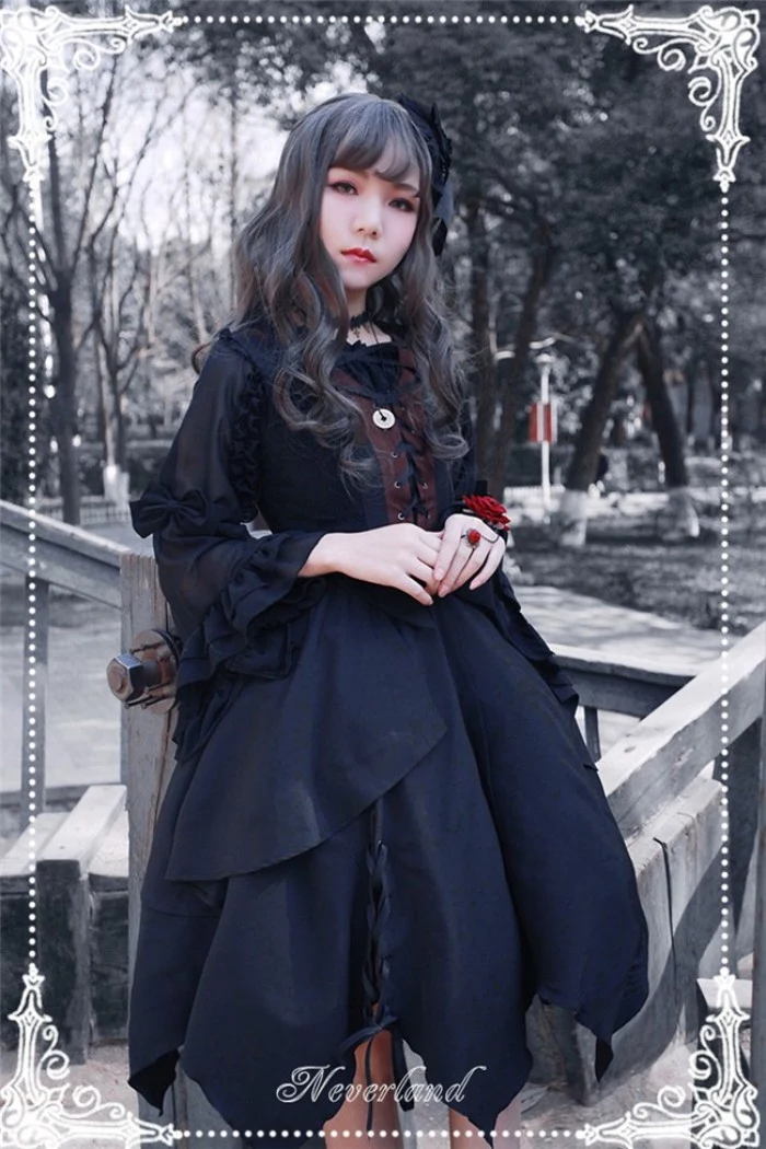 serious looking gir, with dark curled hair, dressed in a black, gothic lolita dress, with a lace up detail, and frilly sheer sleeves