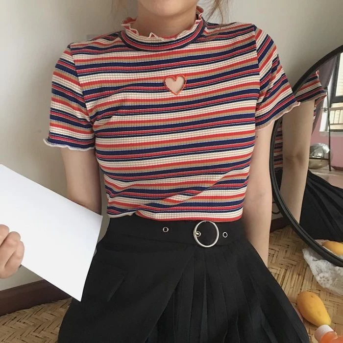 heart-shaped cutout detail, on a striped short-sleeved top, with small frill details on the neck and sleeves, 90s grunge fashion, worn with a belted, pleated black mini skirt