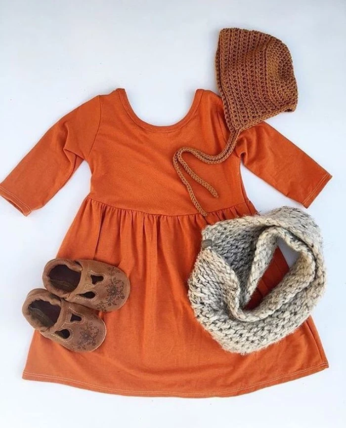 orange jumper dress, with quarter sleeves, toddler thanksgiving outfit, brown suede shoes, an off-white tube scarf, and a brown knitted hat