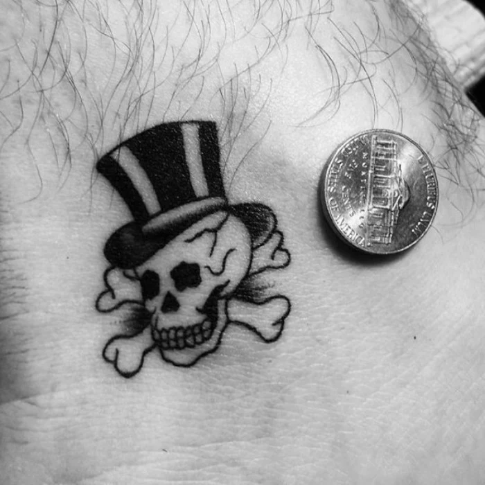 small tattoos with meaning, a skull with a top hat, tattooed in black, on a man's ankle, penny placed next to it for scale, memento mori 