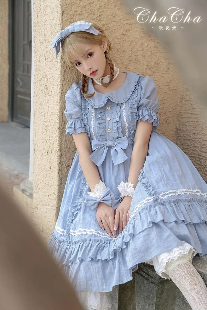 baby blue dress, with lots of frills, a peter pan collar, lace trims and small bows, what is lolita, worn by a slim young woman, with dark blonde pigtails
