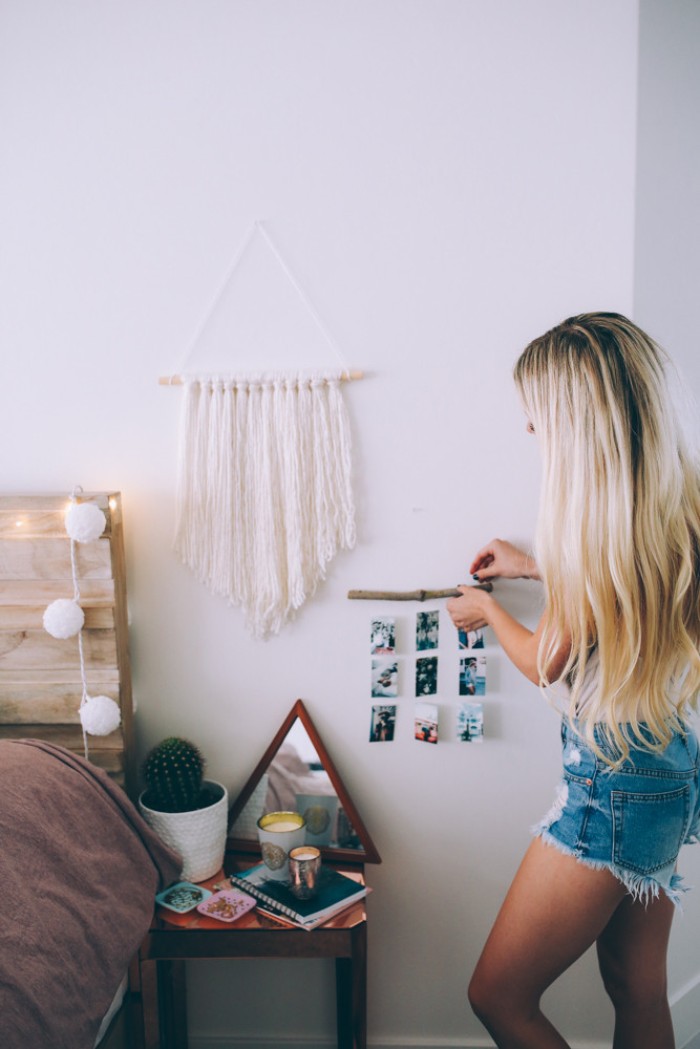 blonde woman with long wavy hair, attaching a small wooden stick, decorated with nine photos, tied on pieces of string, to a white wall, cute teen rooms, marcame wall decoration in white nearby