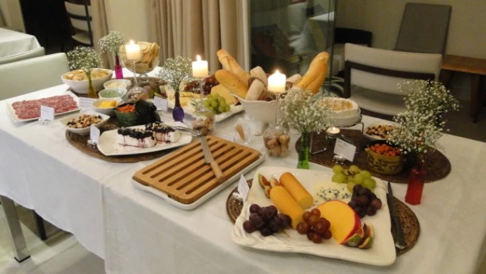 bread basket and a cheese platter, plates with salami and other nibbles, on a table decorated with several small white bouquets, and three lit candles, 50th birthday themes, hosting a wine tasting