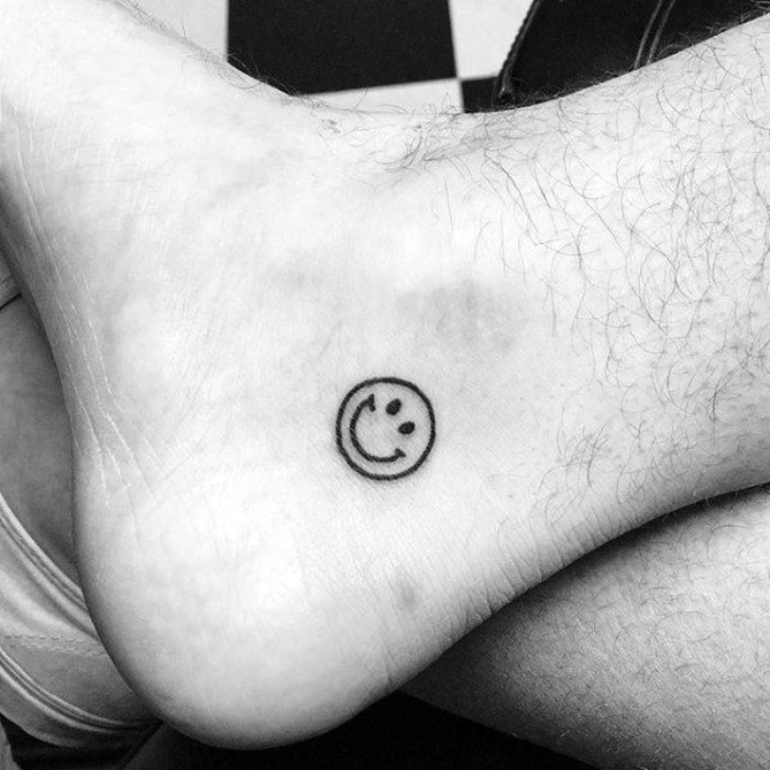 meaningful tattoo ideas, a simple drawing of a smiley face, tattooed in black, on a person's foot, near his sole