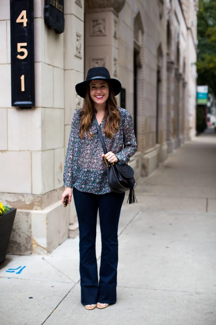 patterned semi-sheer blouse, and slightly flared dark blue jeans, worn by a smiling brunette woman, thanksgiving outfits, with black felt hat, and black cross body bag