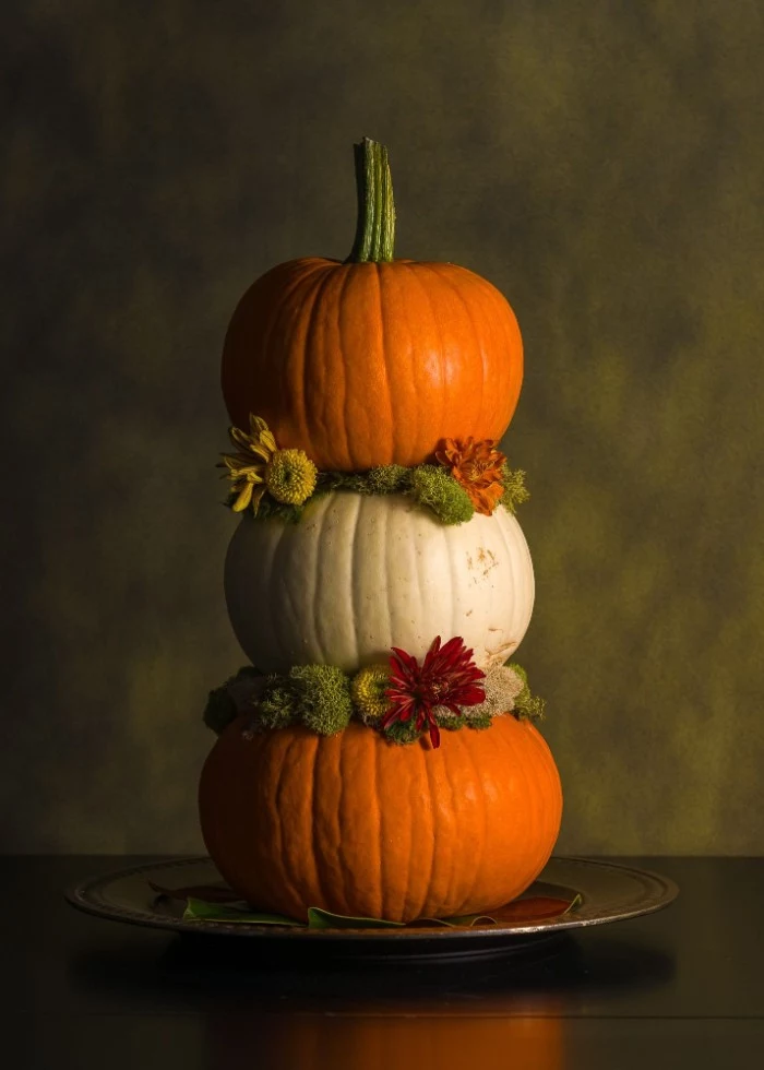tower-like thanksgiving ornament, made from three orange and white stacked pumpkins, decorated with red and yellow flowers, and light green plants