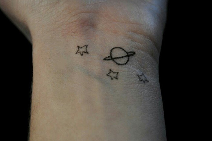 planet with a ring, and three stars, simple but cool arm tattoos, inspired by antoine de saint-exupéry's classic, le petit prince, on a person's wrist, best meaningful tattoo for men