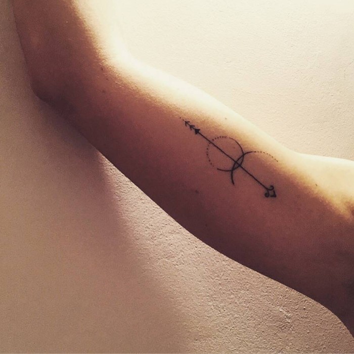 thin arrow with a stylized design, decorated with a circle and a crescent shape, tattooed on a man's upper arm, tattoos with deep meaning, fresh starts and looking at the future