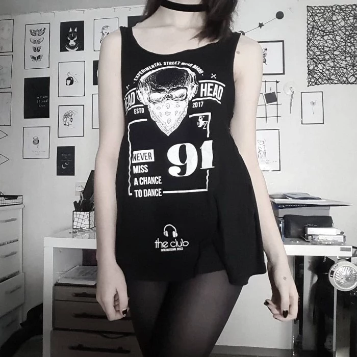 long tank top in black, with white print, worn as a mini dress, over sheer black tights, by a slim and pale, young woman with a black chocker necklace