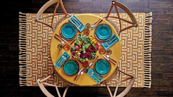 yellow round table, with four seats, featuring teal plates and napkins, thanksgiving dinnerware, centerpiece with fall vegetables