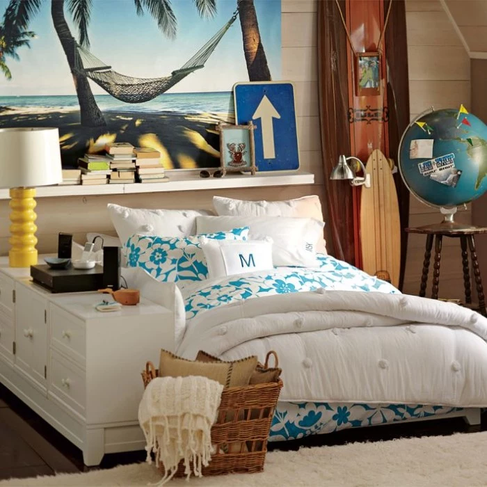floral duvet and pillow covers, in white and teal, on a bed in a spacious room, with surfing boards, and a model globe, large photo of a hammock on a beach, covering one wall, cool beds for teens