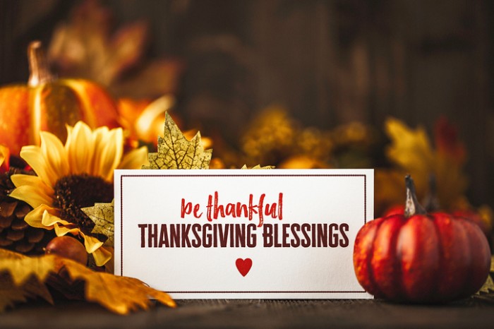 be thankful thanksgiving blessing, written in red and dark brown, on a white card, surrounded by small pumpkins, fall leaves and a sunflower, thanksgiving greetings